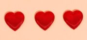 Three red hearts on a peach background symbolizing love and romance.